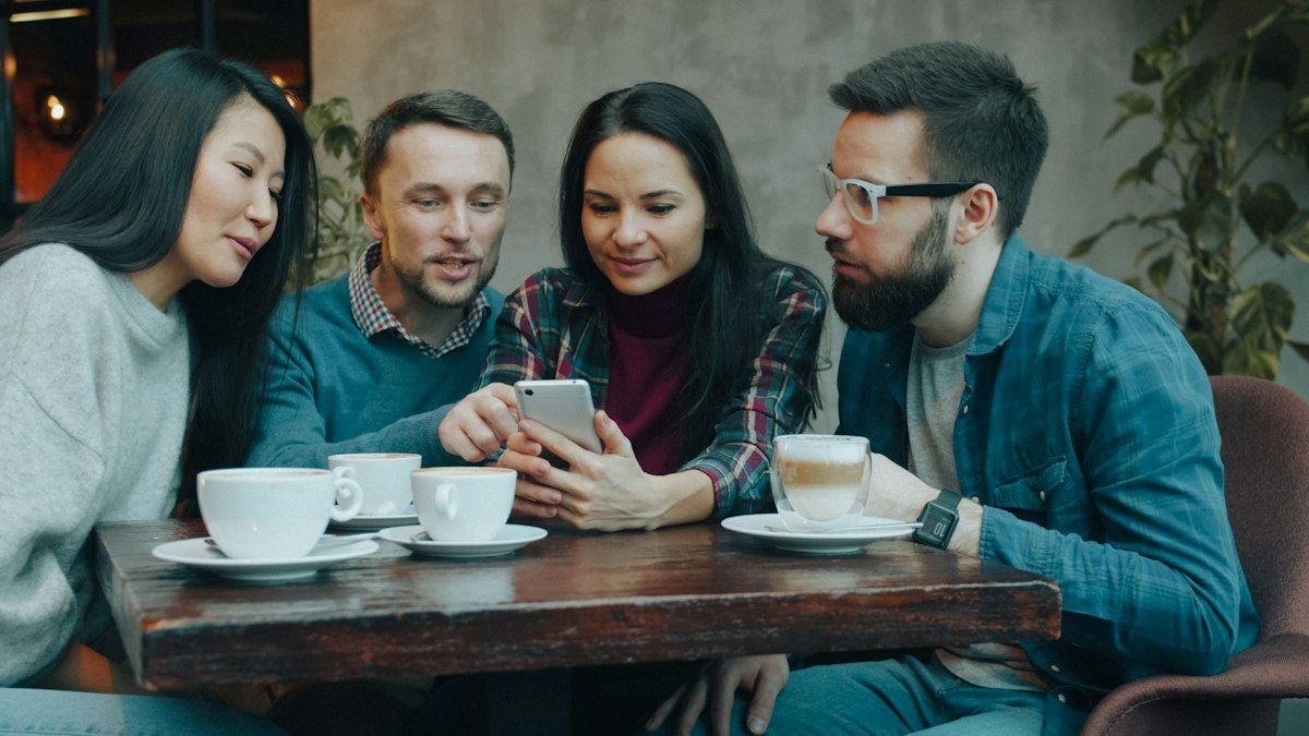 Sekelompok teman melihat satu smartphone bersama di meja kafe