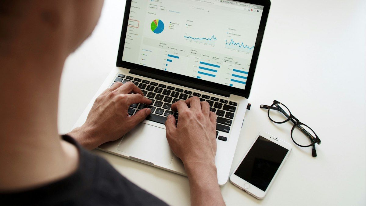 Seseorang mengetik di laptop dengan dashboard grafik di layar