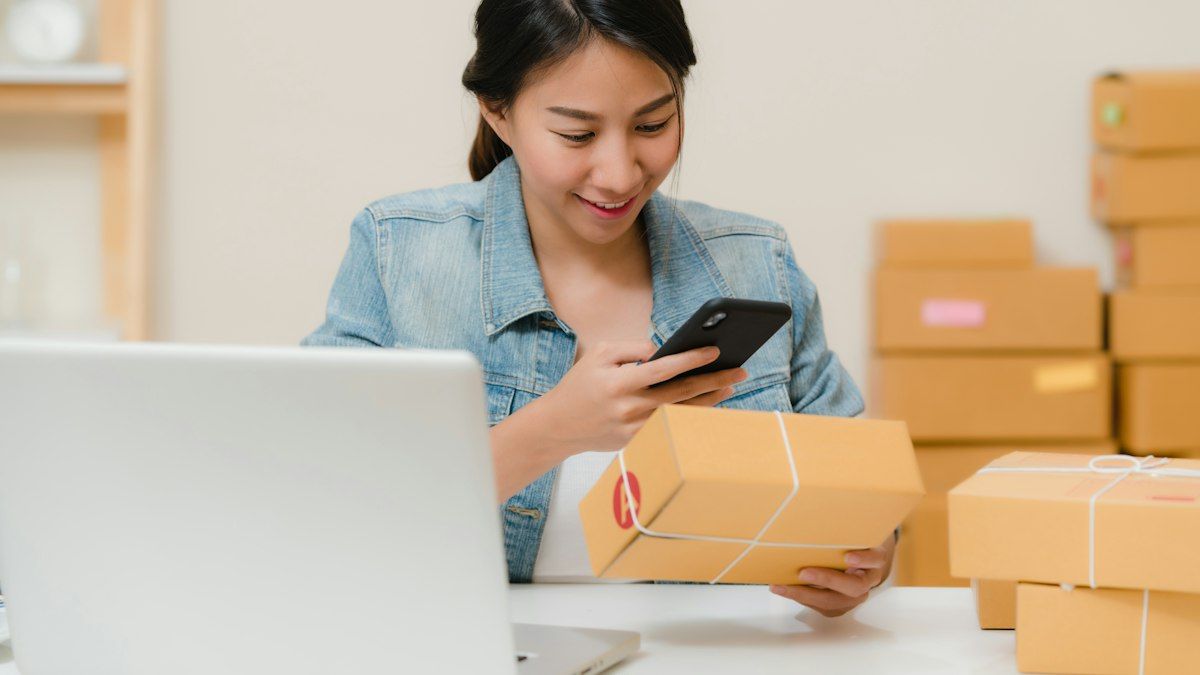 Penjual online tersenyum memotret paket pesanan dengan smartphone