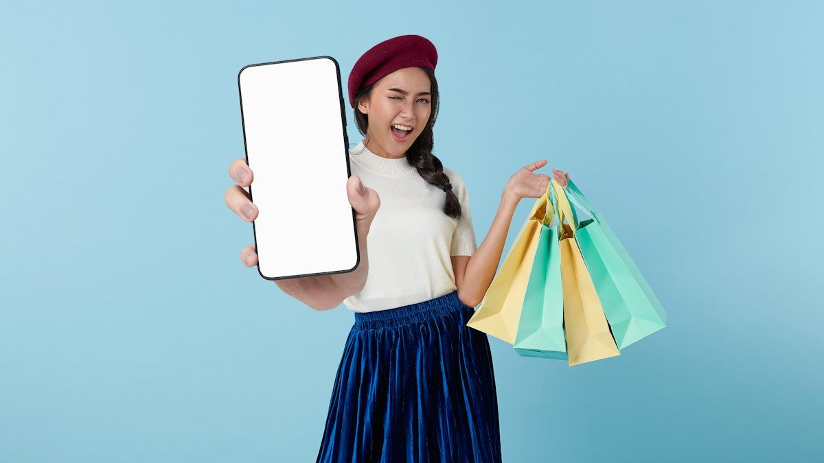 Perempuan memegang smartphone dan tas belanja dengan latar biru