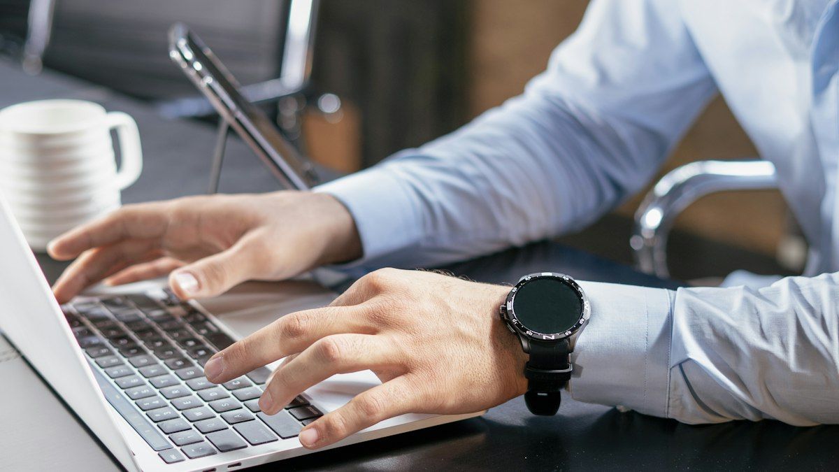 Seseorang mengetik di laptop dengan jam tangan di pergelangan