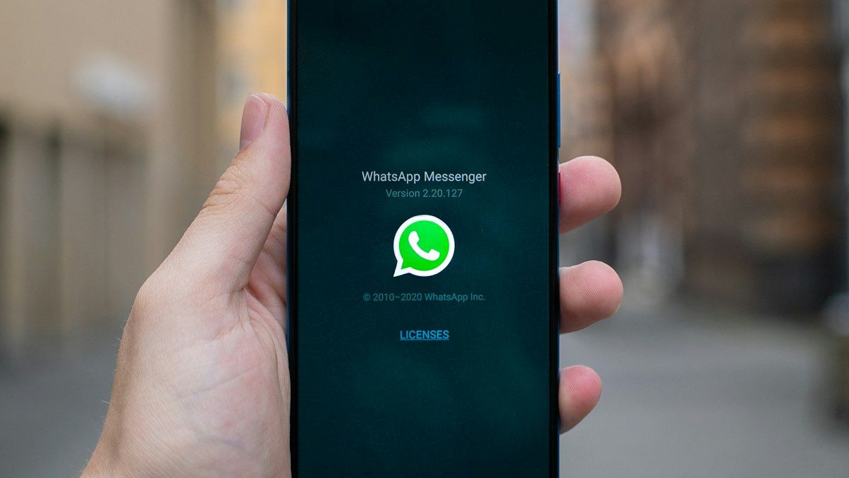 A hand holding a smartphone showing the WhatsApp app