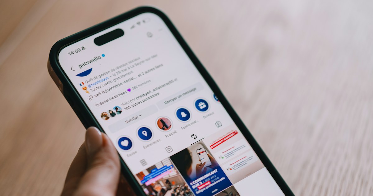 Tangan memegang smartphone yang menampilkan feed media sosial
