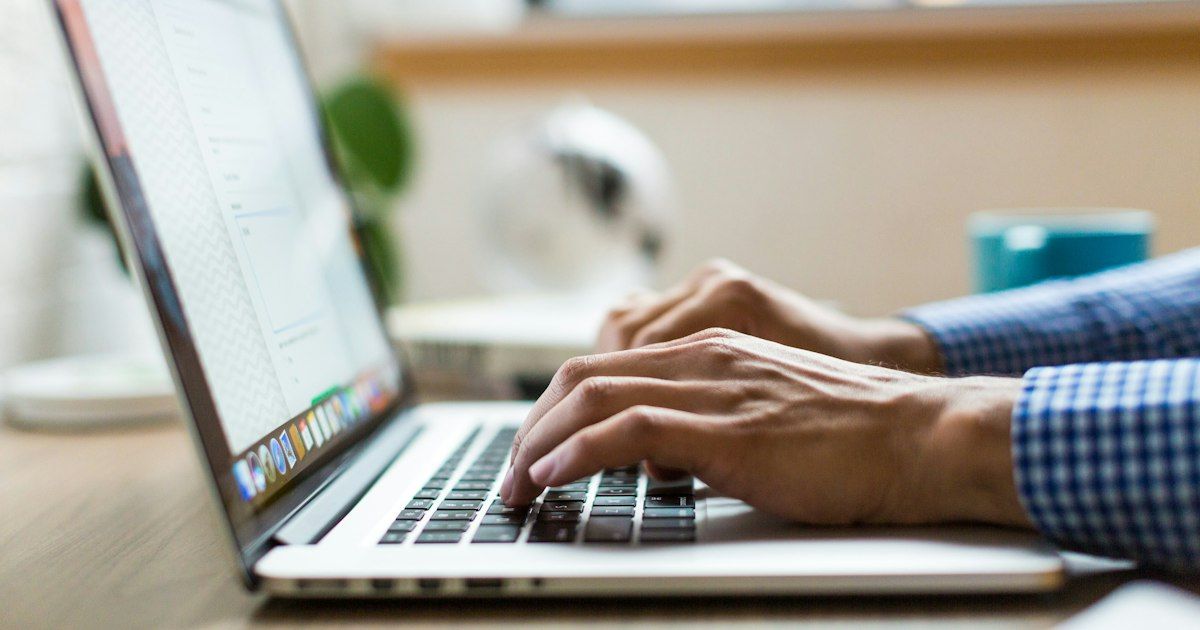 Tangan mengetik di laptop di atas meja kerja
