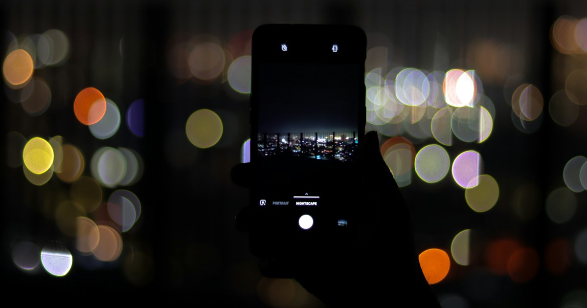 Smartphone menyala di malam hari dengan latar lampu bokeh