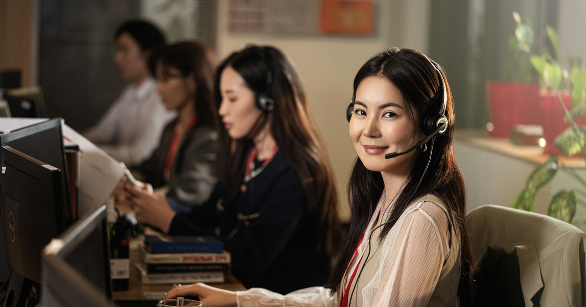 Agen customer service tersenyum memakai headset sambil membalas chat pelanggan